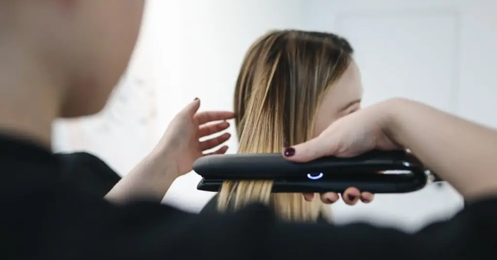 Close-up of a hairstylist using a straightening iron for sleek hairstyle indoors.